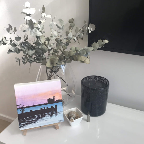 Painting on easel in home setting of Newcastle harbour foreshore at sunset from the jetty with coal towers in background